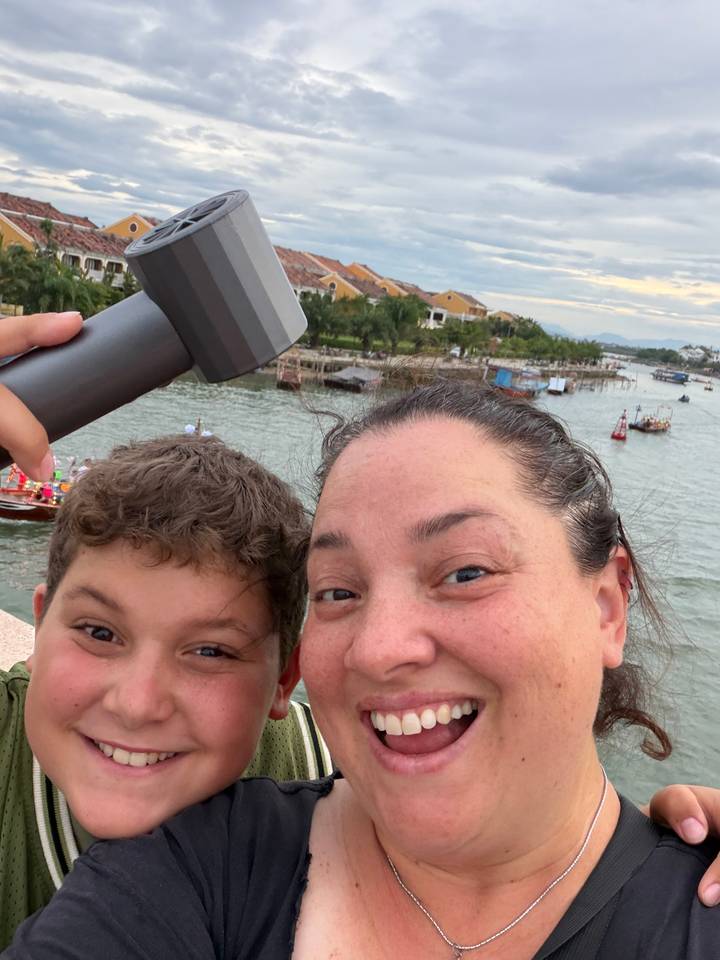 Mother and son smiling on a bridge overlooking a lively river scene with boats