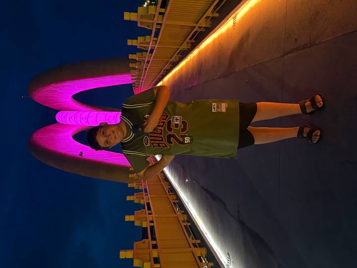 Boy posing confidently on an illuminated bridge glowing pink against the night sky