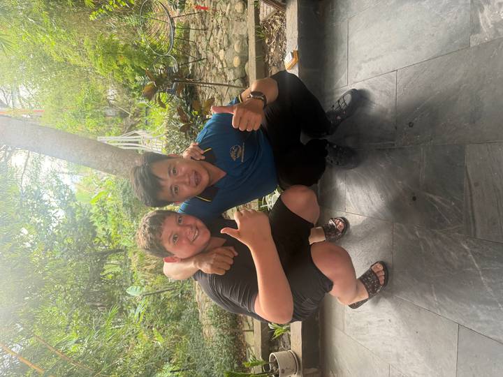 Young traveler and local guide crouching together with thumbs up in a garden area