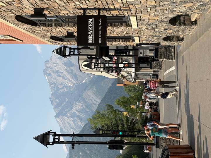 Pedestrian street in a mountain town with shops, visitors, and a dramatic rocky peak rising behind.