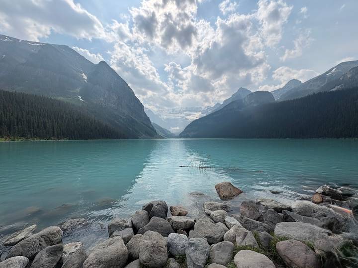 Wide panorama of an emerald lake nestled between steep forested mountains under a textured sky.