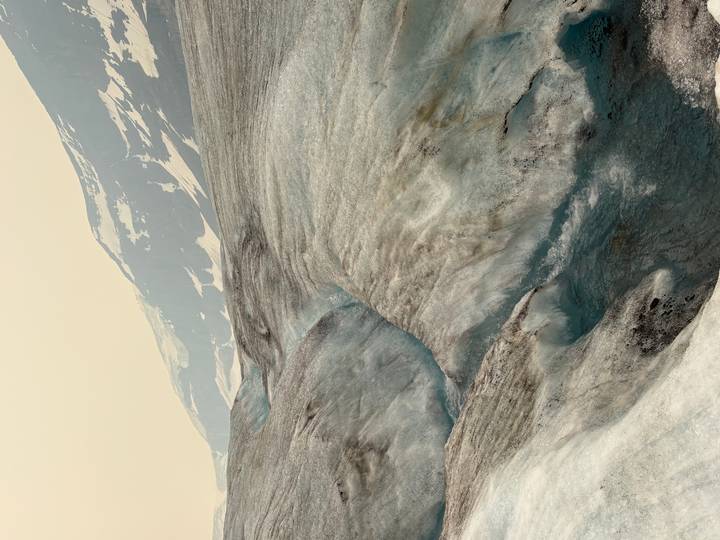Expansive glacier landscape with winding meltwater channels and distant snow-capped ridges.