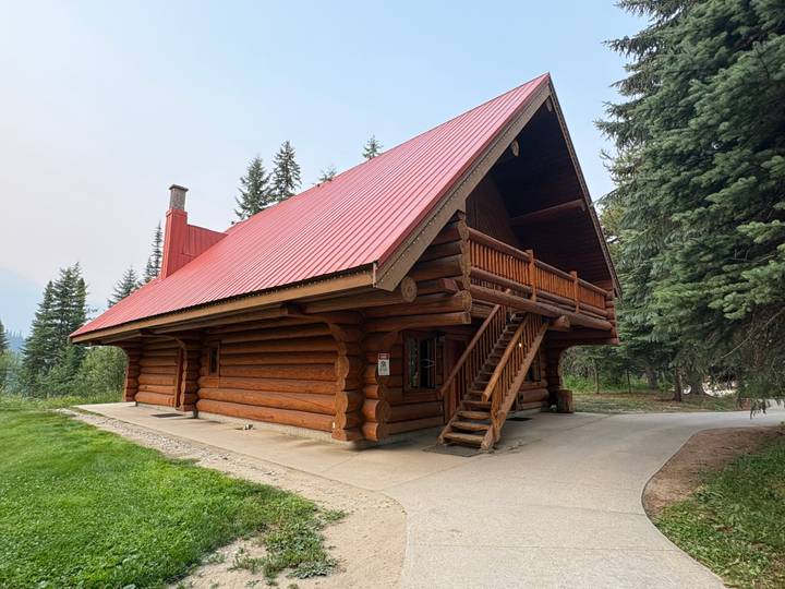 Rustic log cabin with a steep red roof nestled among conifer trees.