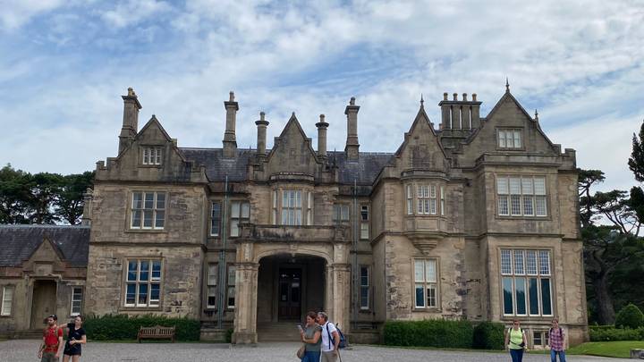 Historic manor house with ornate chimneys and visitors exploring the entrance courtyard.