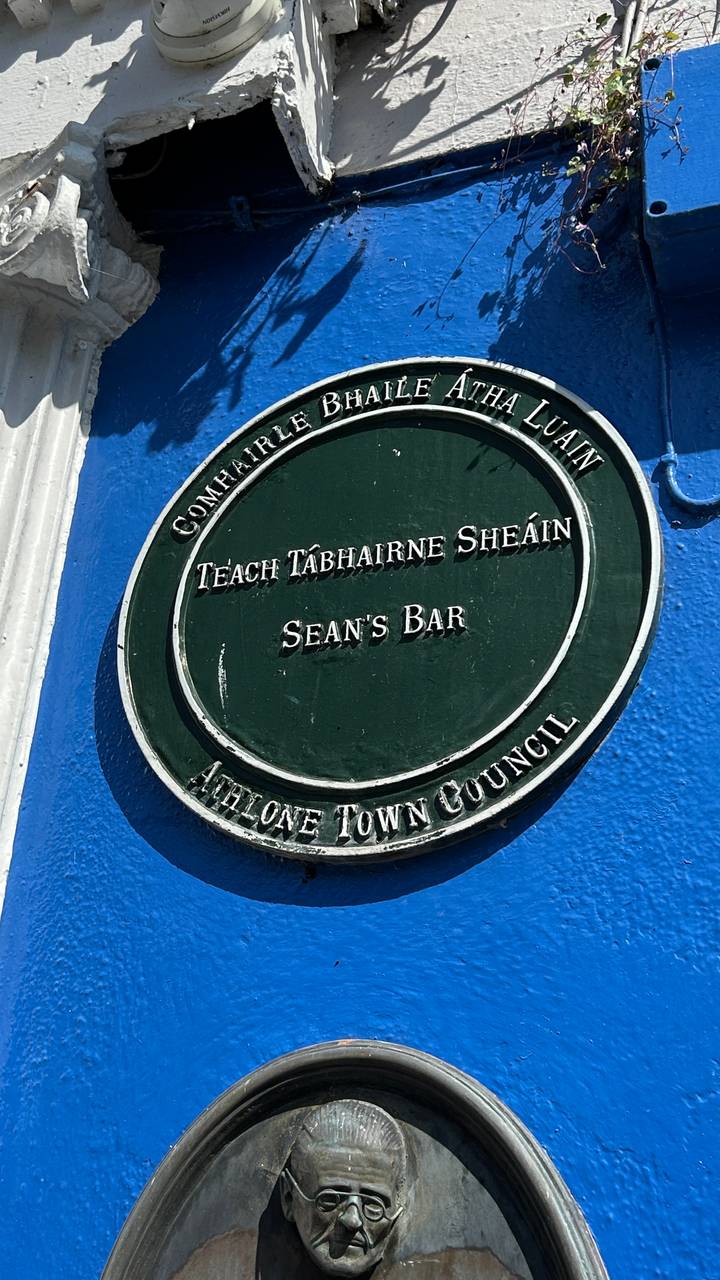 Close-up of a green heritage plaque for Sean's Bar mounted on a bright blue wall.