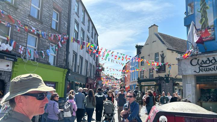 Festive pedestrian street in Galway decorated with flags, crowded with shoppers and tourists.