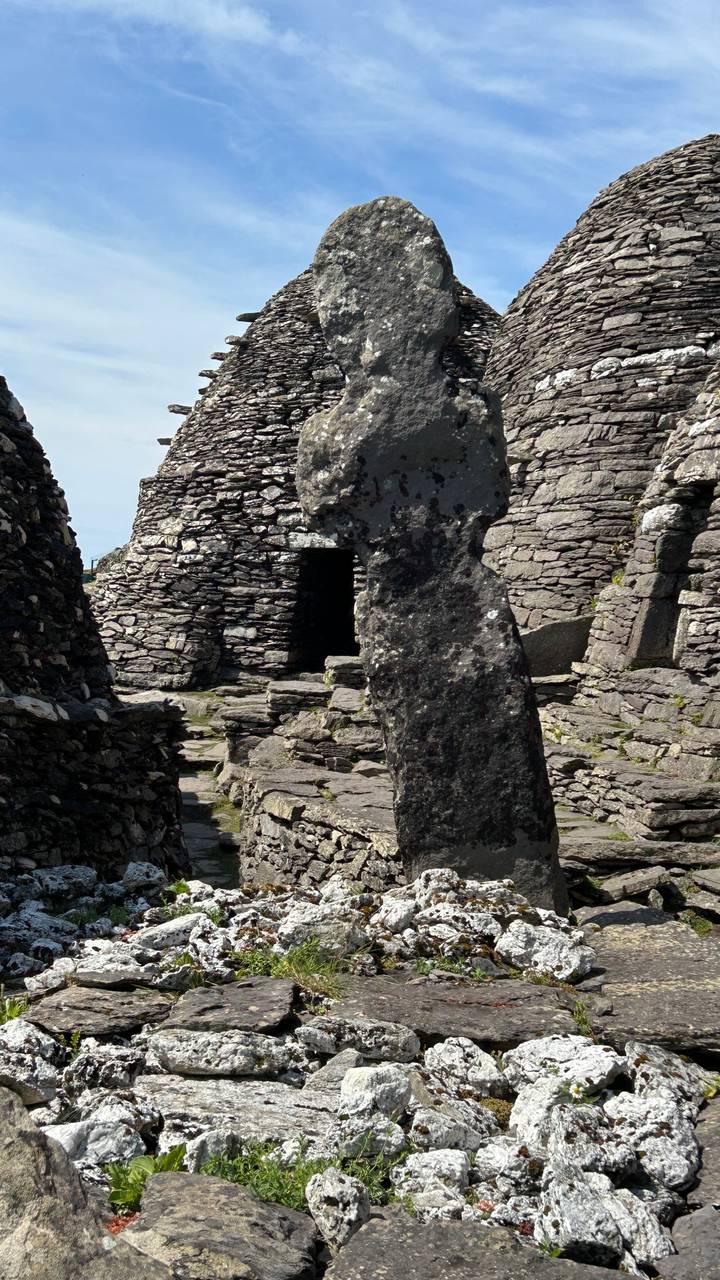 Ancient dry-stone beehive huts and a weathered stone pillar on a rocky island site.