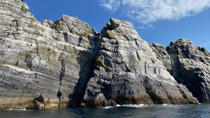 Towering grey sea cliffs rise sharply from deep blue Atlantic waters under a clear sky.
