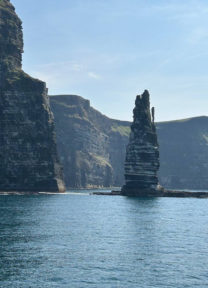 Tall sea stack stands beside the dramatic layers of the Cliffs of Moher.