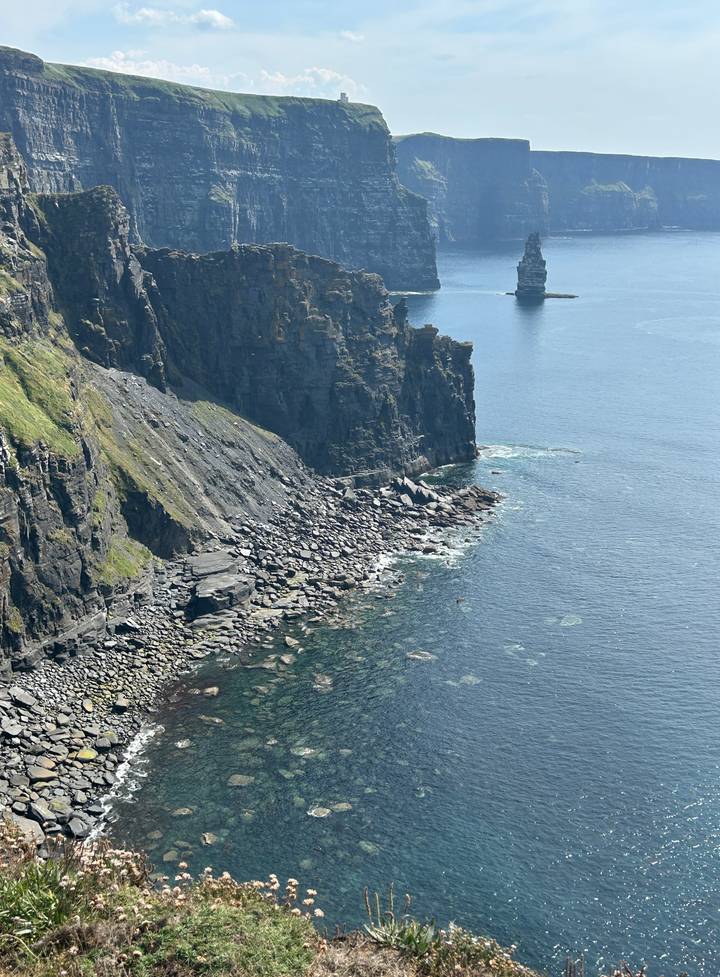 Steep green-topped cliff plunges into clear Atlantic waters along Ireland's rugged coast.