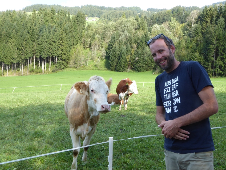 Man posing with cows in a grassy field.
