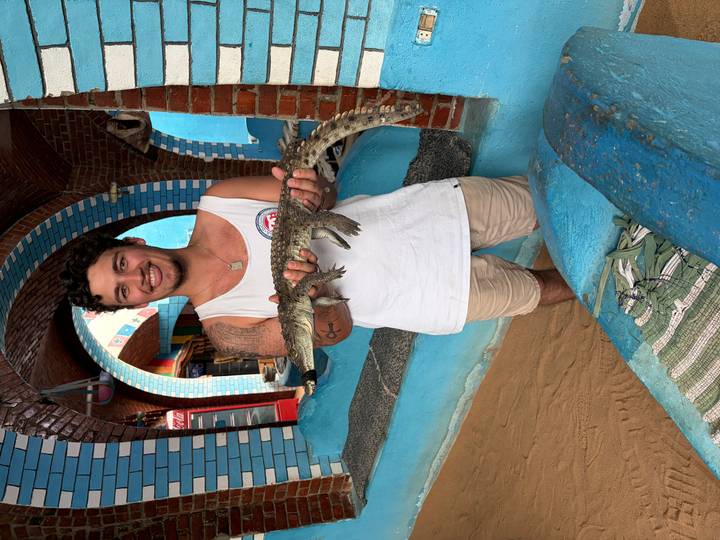 Traveller smiling while holding a small crocodile inside a colourfully tiled Nubian house.