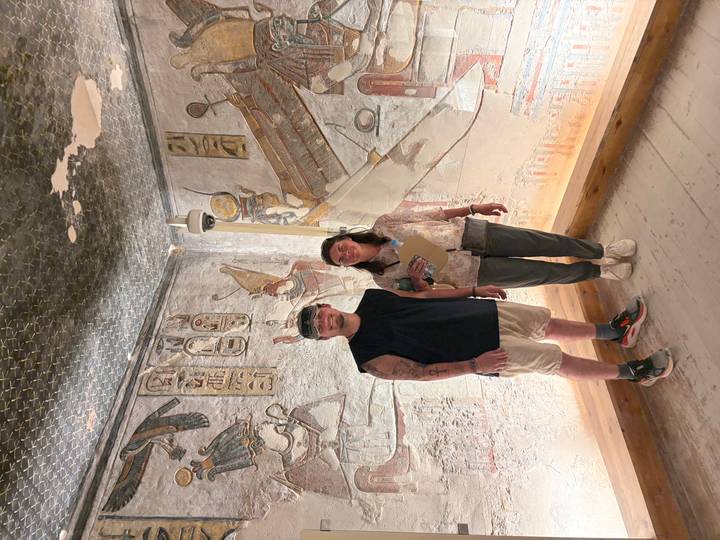 Two travellers inside a vividly painted tomb chamber with hieroglyphs in the Valley of the Kings.