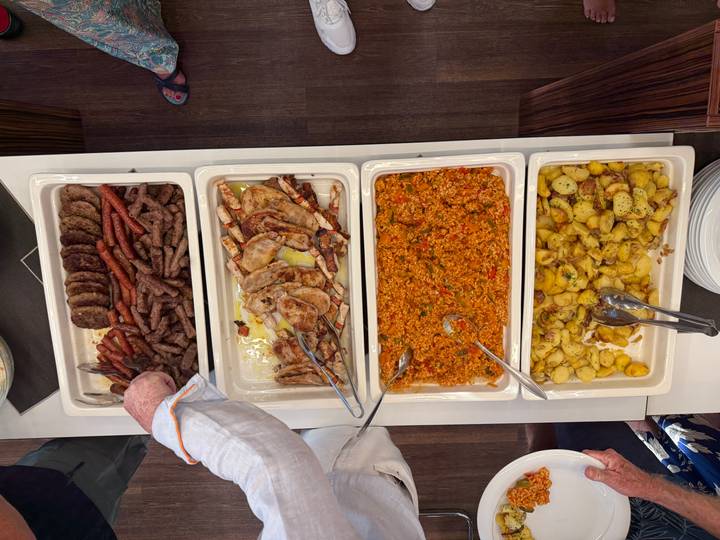 Overhead view of buffet trays filled with grilled meats, rice, and roasted potatoes being served.