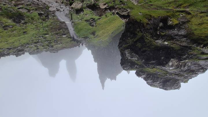 Misty view of jagged rock pinnacles and hikers on a rugged trail at the Old Man of Storr on the Isle of Skye.