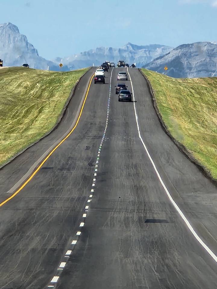 Long straight highway with a single car driving away between grassy shoulders.