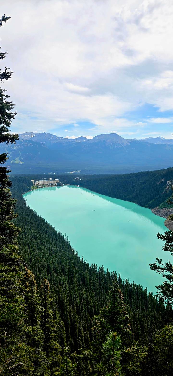 Elevated view of Lake Louise's turquoise expanse and iconic shore hotel nestled in forest.