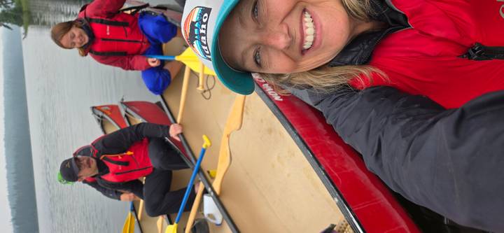 Selfie of paddlers in red canoes on calm water dressed in life jackets and smiling.