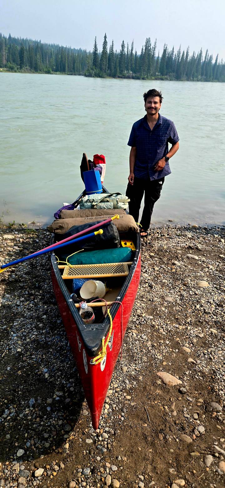Canoe beached on a pebbled shore packed with dry bags, paddles and camping equipment next to turquoise water.