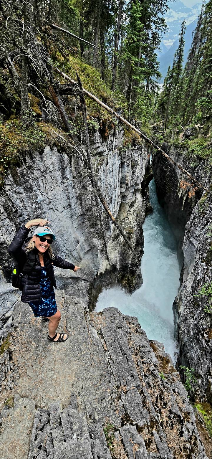 Smiling woman points toward a deep turquoise gorge carved through grey limestone walls.