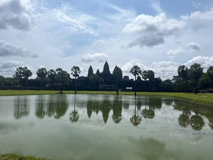 Reflection of the Angkor Wat towers in a calm moat beneath a partly cloudy sky.