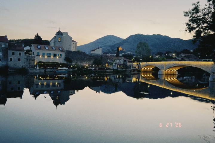Twilight scene of a stone bridge and riverside village reflected perfectly in calm water.