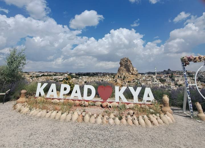 Lavender-lined lookout with large “KAPADOKYA” sign and heart symbol facing the rock citadel of Uchisar.
