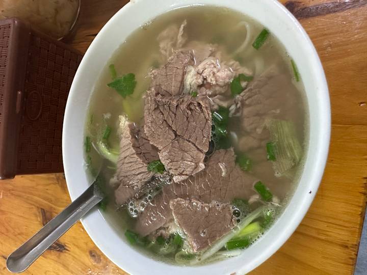 Steaming bowl of Vietnamese pho with sliced beef, herbs and clear broth on a wooden table.