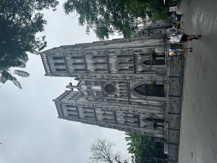 Gothic-style St. Joseph’s Cathedral towers over visitors walking past its weathered grey façade in Hanoi.