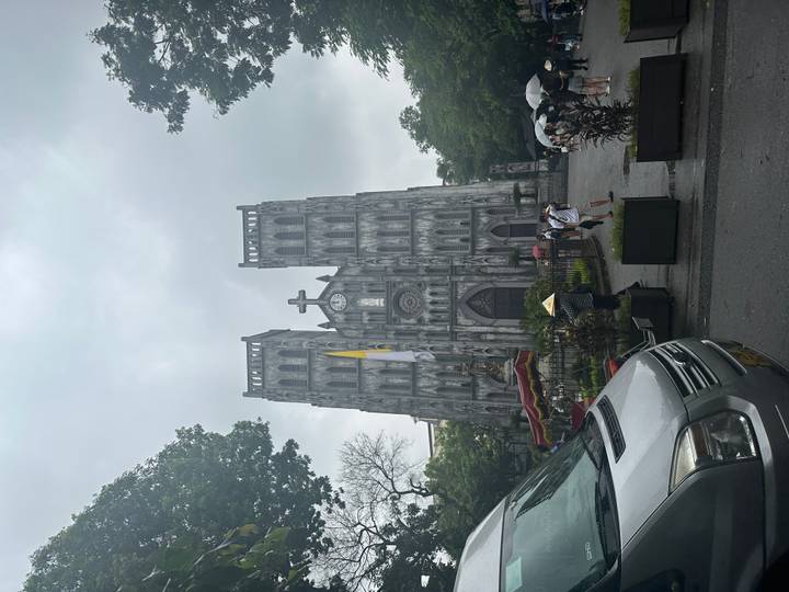 Front view of the grey neo-gothic cathedral with visitors and a parked van in the foreground