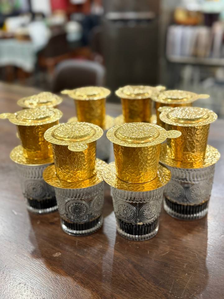 Row of ornate golden phin filters placed on patterned glasses ready for brewing Vietnamese coffee.