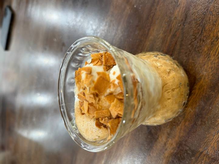 Dessert glass filled with whipped egg coffee topped with crunchy flakes on a wooden table.