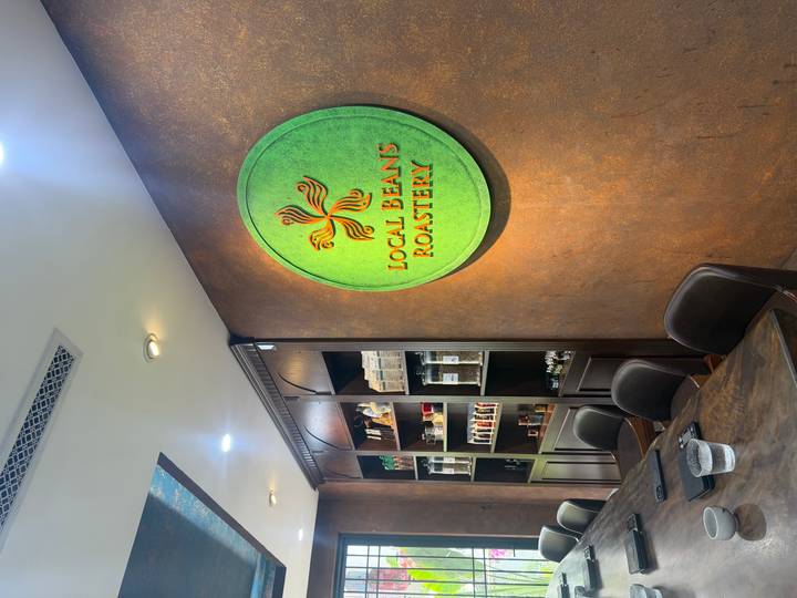 Interior of a modern café roastery with shelves of coffee products and a round green sign reading Local Beans Roastery.