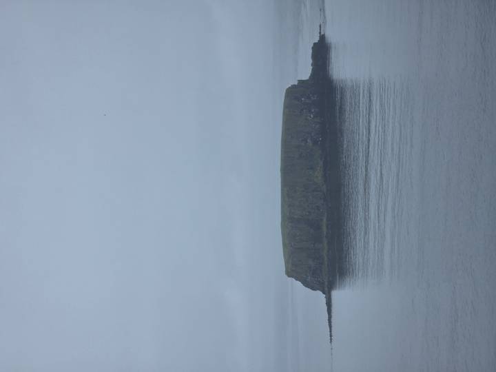 Low, flat-topped island rising from a misty grey sea under overcast skies.
