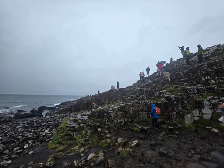 Visitors climb hexagonal basalt columns at the Giant’s Causeway on a drizzly day.
