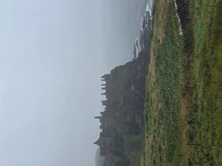 Ruins of a cliff-top stone castle loom through coastal fog above rough seas.