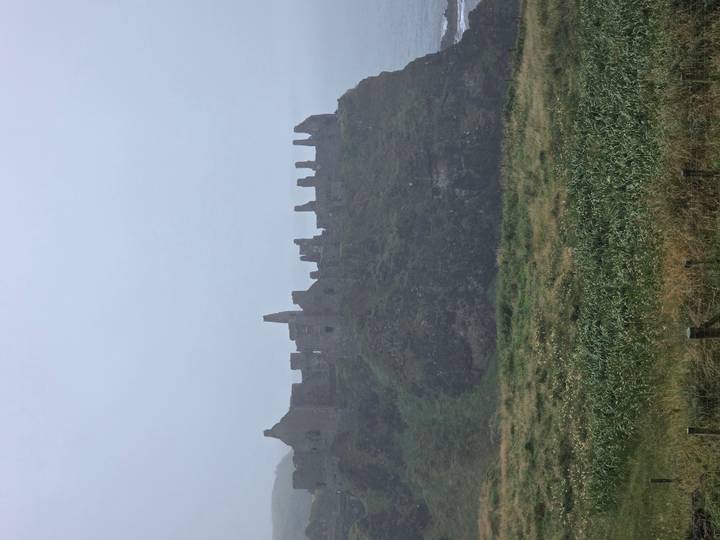 Closer view of the weathered stone ruins of Dunluce Castle perched on a grassy cliff.