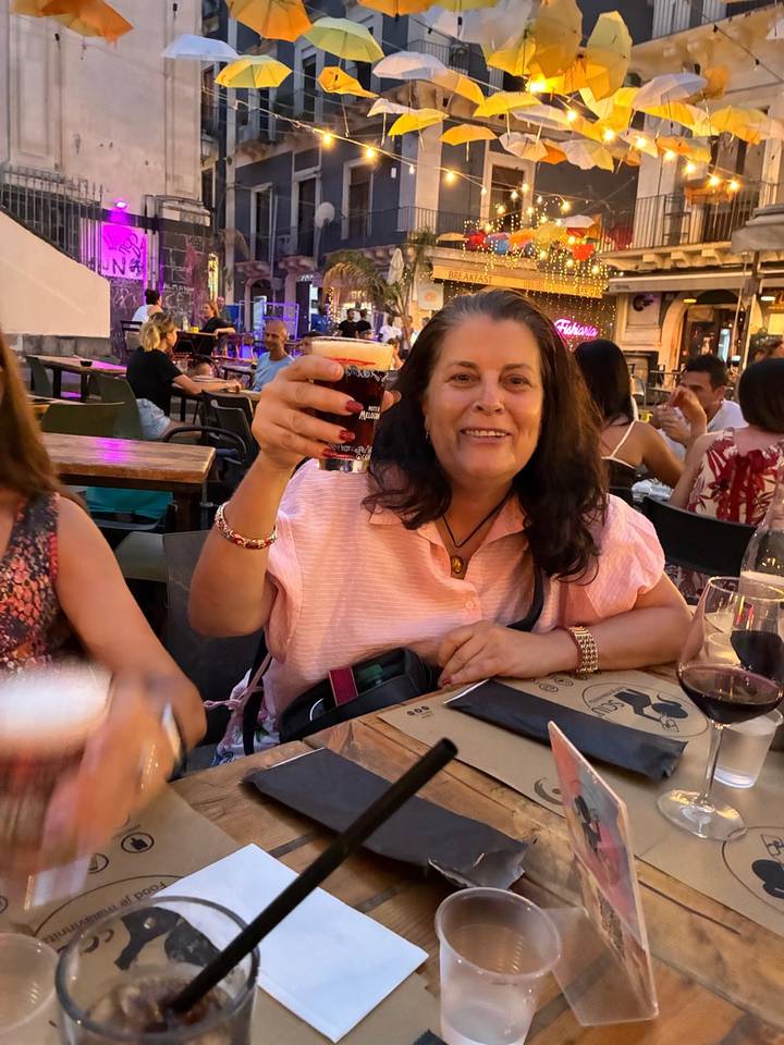 Woman lifting a red cocktail while seated at an outdoor evening cafe, with other diners and warm ambient lighting in the background