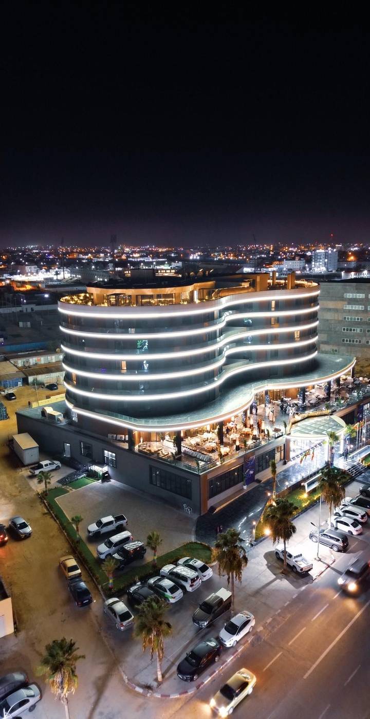 Night aerial of a modern wave-shaped building outlined with bright LED strips and lively rooftop dining