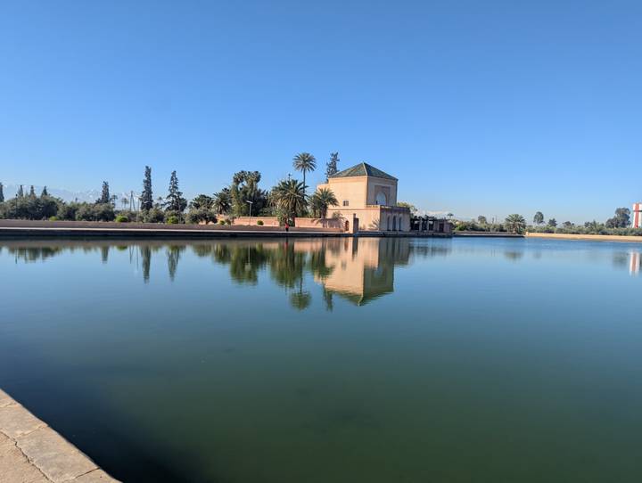Pavilion of Marrakesh’s Menara Gardens reflected perfectly in a serene rectangular pool on a clear morning.