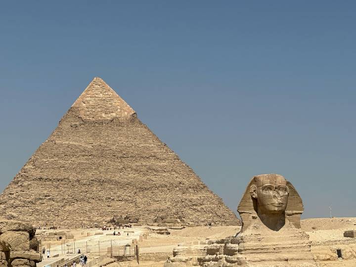 Classic view of the Great Pyramid of Giza with the Sphinx in the foreground against a clear blue sky.