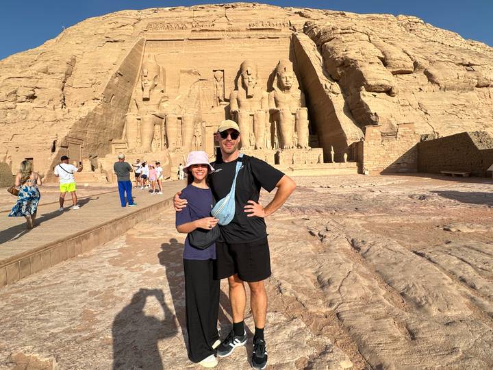 Tourists posing in front of Abu Simbel's colossal statues carved into the sandstone cliff.