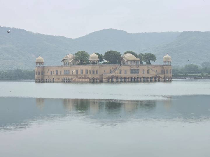 Jal Mahal palace floating in calm lake with misty hills in background.