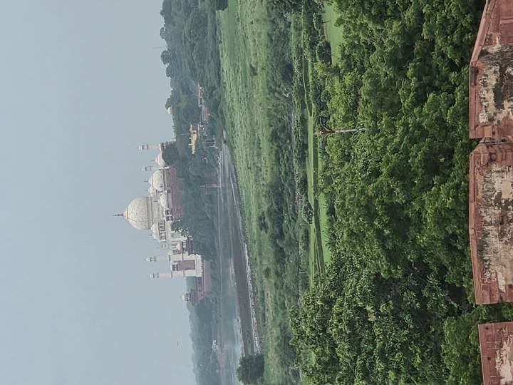 Distant lateral view of Taj Mahal across lush green Yamuna floodplain.