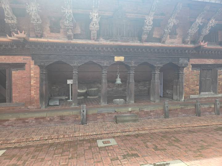 Brick and timber courtyard with bell and traditional Nepalese carvings partly veiled by mist.