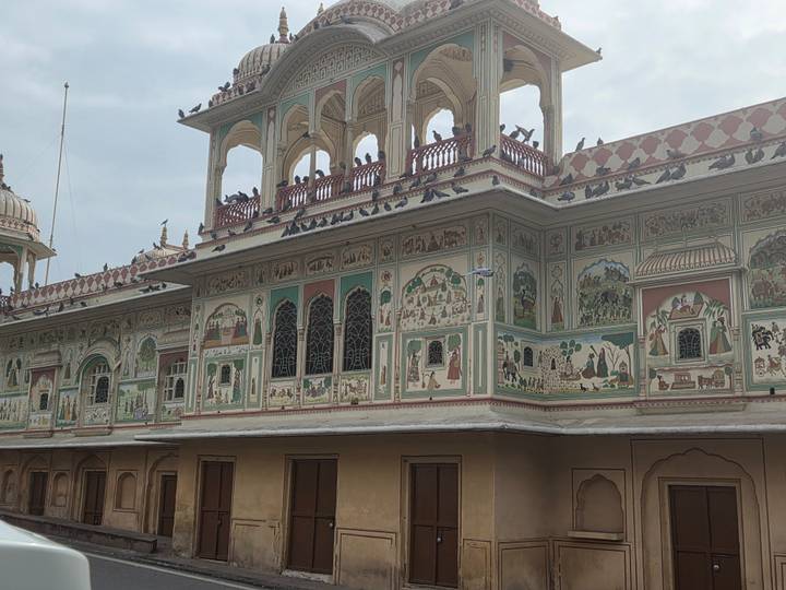 Exquisitely painted facade of Jaipur City Palace with numerous pigeons perched on arches.