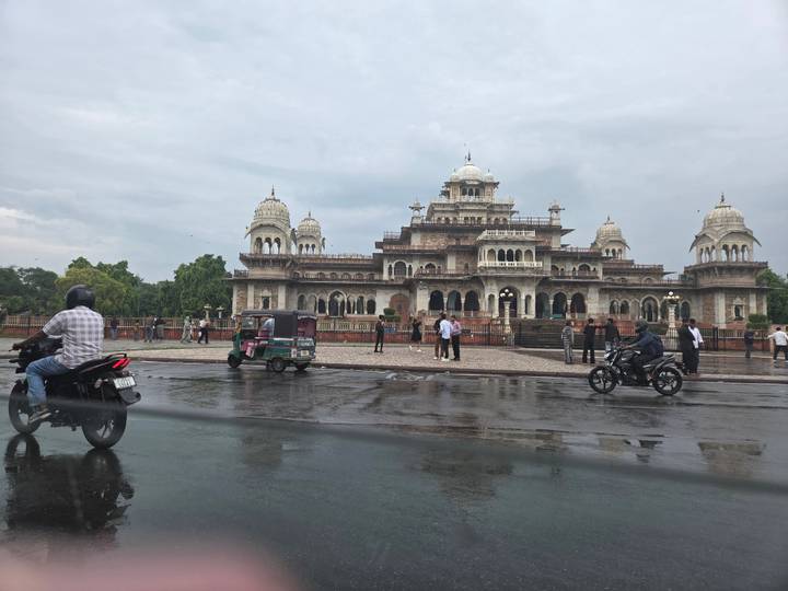 Albert Hall Museum Jaipur viewed across wet street with passing motorbikes and rickshaw.