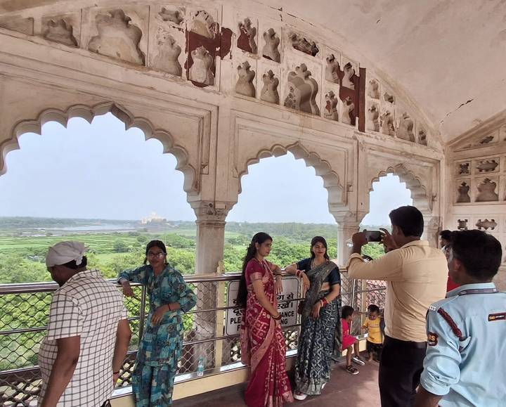 Tourists admire river views through ornate Mughal arches inside a historic fort.