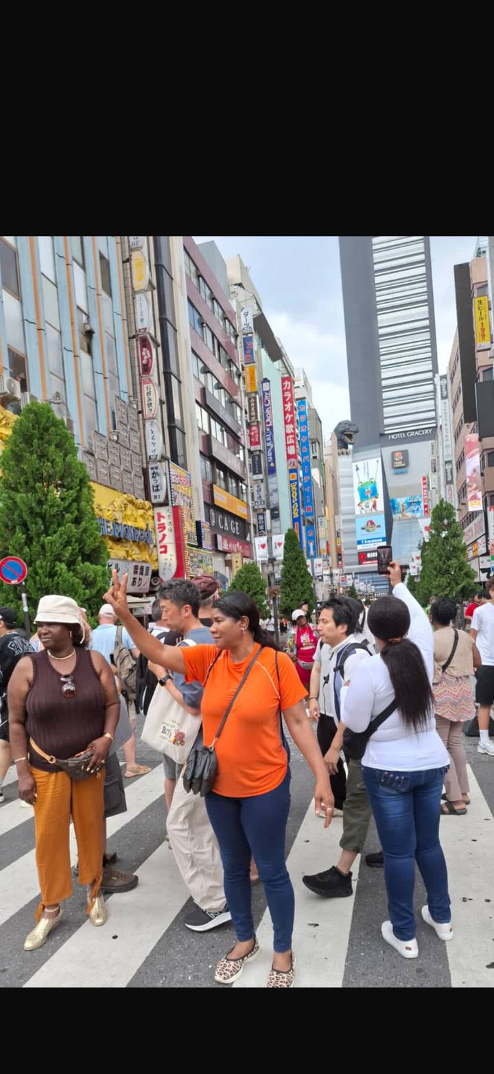 Bustling Shinjuku street filled with neon signs, shoppers and the iconic Godzilla head peeking above buildings.