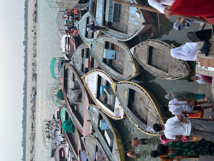 Many wooden rowboats moored along busy riverside ghat with people preparing to board